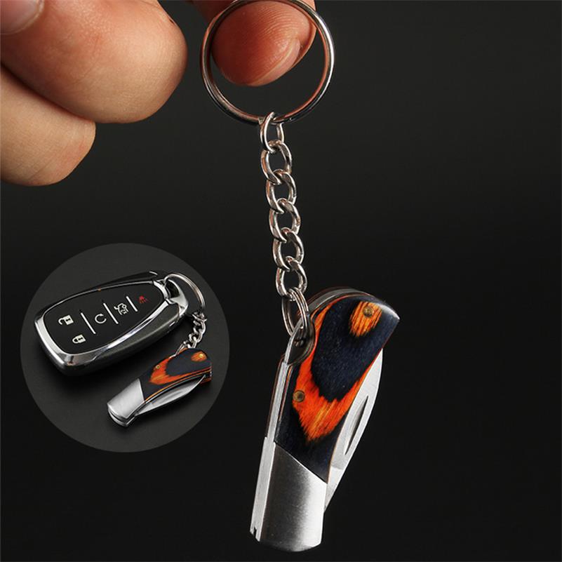 A closed mini folding keychain knife hangs from a silver key ring and chain, its handle a navy-and-orange coloured wood with a silver bolster, plus an inset showing it beside a car key fob for scale.