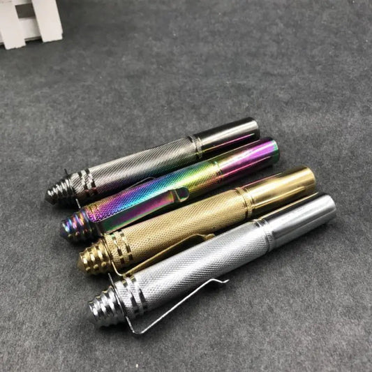 Four pen-style batons in gunmetal, rainbow, gold, and silver finishes arranged diagonally on a dark felt surface, showing the knurled grip, conical tip, and pocket clip.