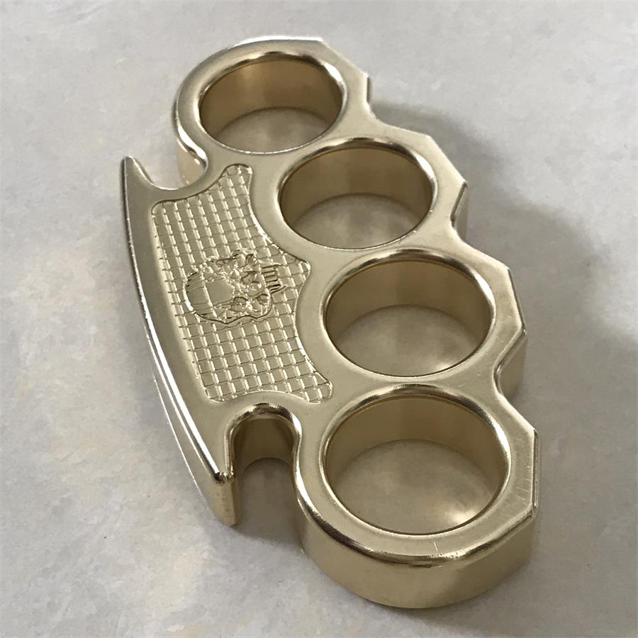 Angled view of the brass mini knuckle duster on a marble surface, skull panel on the left side