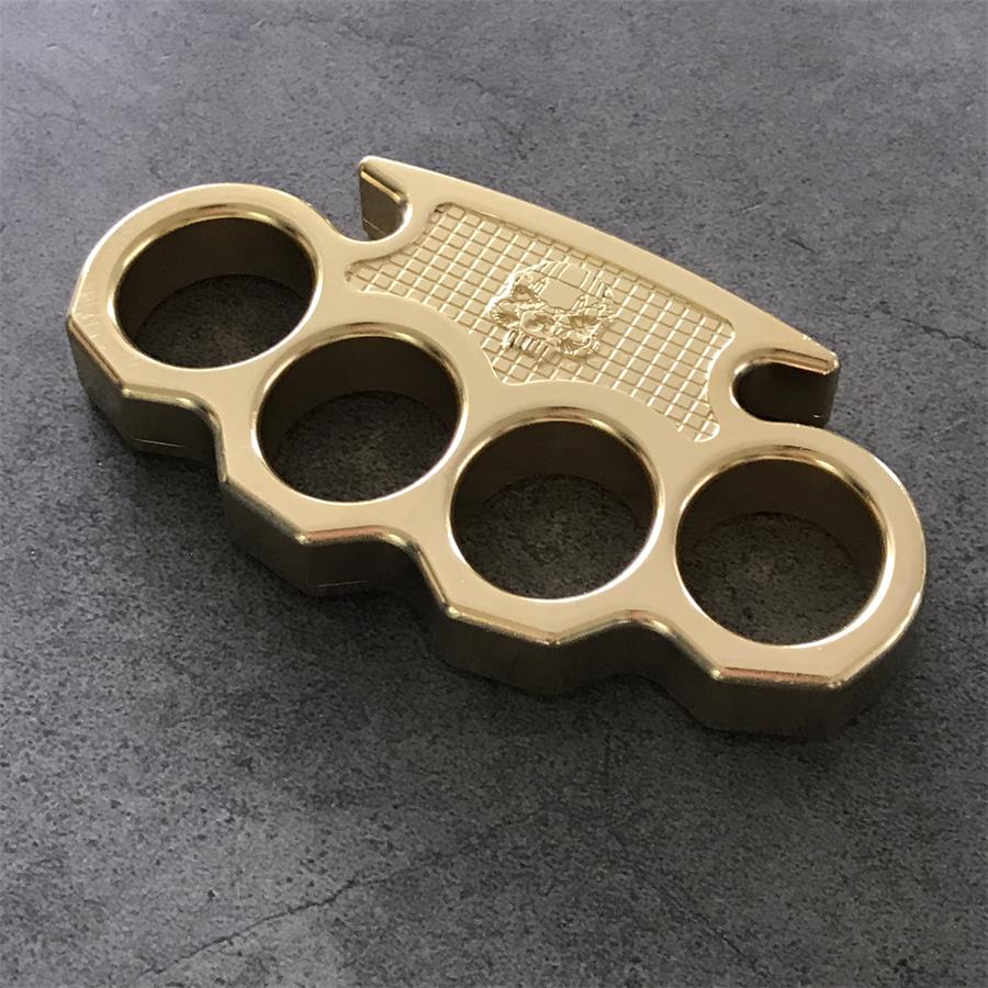 Brass mini knuckle duster displayed on a dark textured concrete surface, showing the full silhouette and finger holes