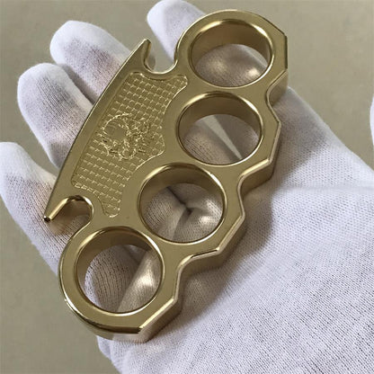 Front view of the brass mini knuckle duster held upright, showing the notched upper edge and pointed lower tip