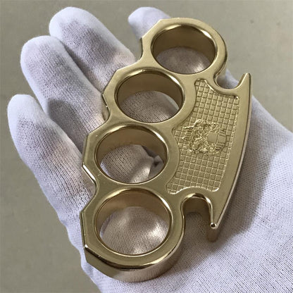 Polished brass mini knuckle duster held in a white-gloved hand, showing the embossed skull checkered panel and four finger holes