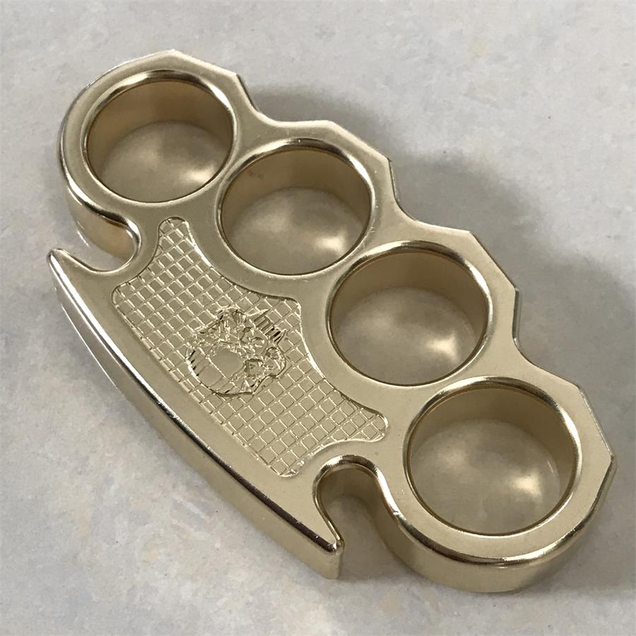 Brass mini knuckle duster on a pale stone surface at an angle, highlighting the grid-textured panel and polished finish