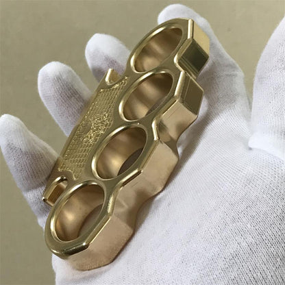 Brass mini knuckle duster resting on an open gloved palm, embossed skull panel facing the camera