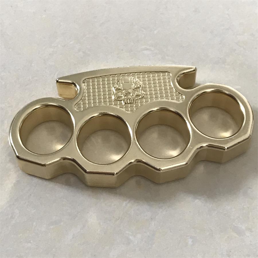 Top-down view of the brass mini knuckle duster on pale stone, showing all four round finger holes