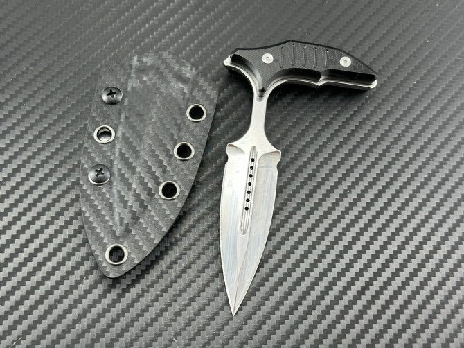 Mirror polish push dagger next to its carbon fiber sheath on textured background