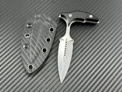 Mirror polish push dagger next to its carbon fiber sheath on textured background