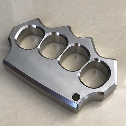 Angled flat lay of the mirror polished four-hole stainless steel knuckle duster showing beveled edges.