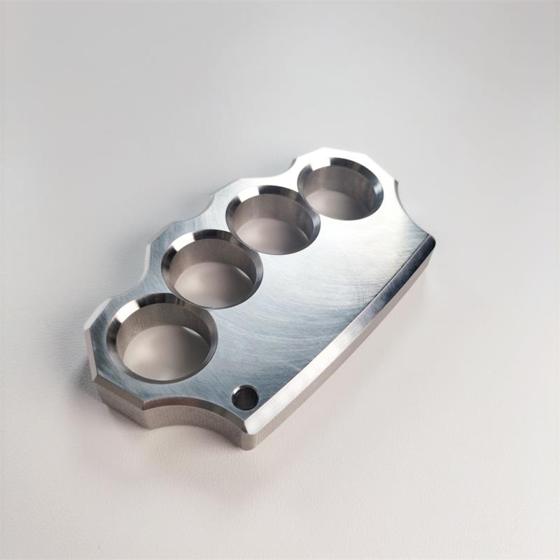 Mirror polished 304 stainless steel four-hole knuckle duster lying flat on a light grey surface, angled front view.