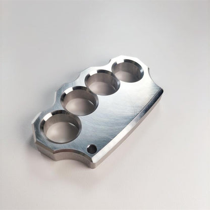 Mirror polished 304 stainless steel four-hole knuckle duster lying flat on a light grey surface, angled front view.