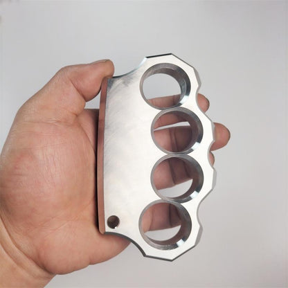 Hand holding the mirror polished four-hole stainless steel knuckle duster, palm-side view showing finger holes.