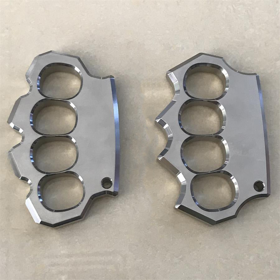 Two mirror polished four-hole stainless steel knuckle dusters placed side by side on a beige surface.