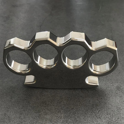 Angled view of the mirror-polished steel knuckle duster on a gray concrete surface, palm panel to the right