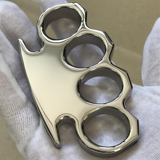 Mirror-polished steel knuckle duster held in a white-gloved hand, showing the four finger holes and stepped angular frame