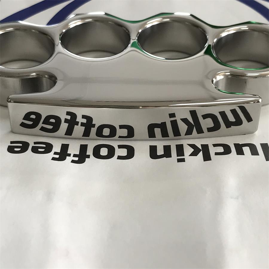 Gloved hand holding the mirror-polished steel knuckle duster, pointed lower tip and stepped shoulders in view