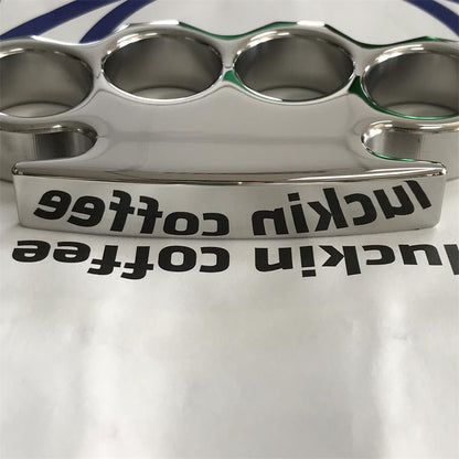 Gloved hand holding the mirror-polished steel knuckle duster, pointed lower tip and stepped shoulders in view