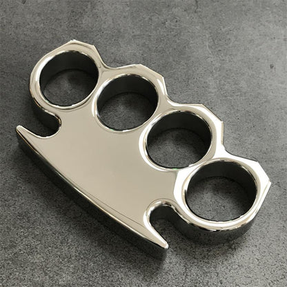Rear-side view of the steel knuckle duster on gray concrete showing the palm-side face and pointed tip