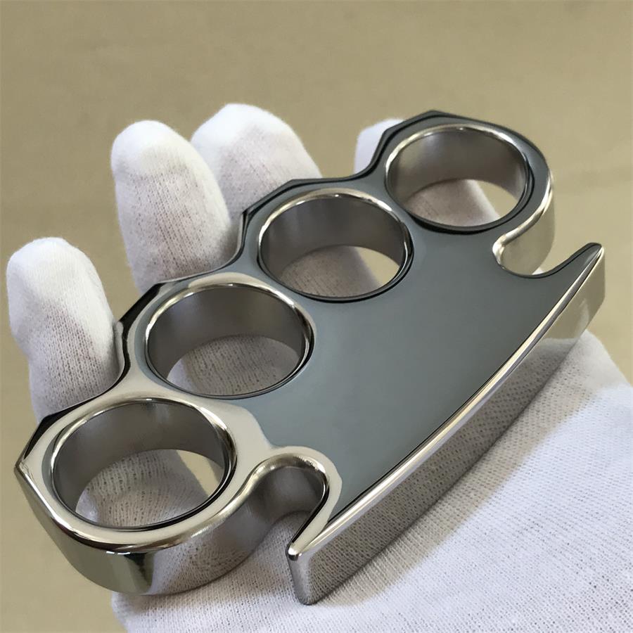 Top-down angled view of the mirror-polished steel knuckle duster held in gloved fingers, four finger holes in frame