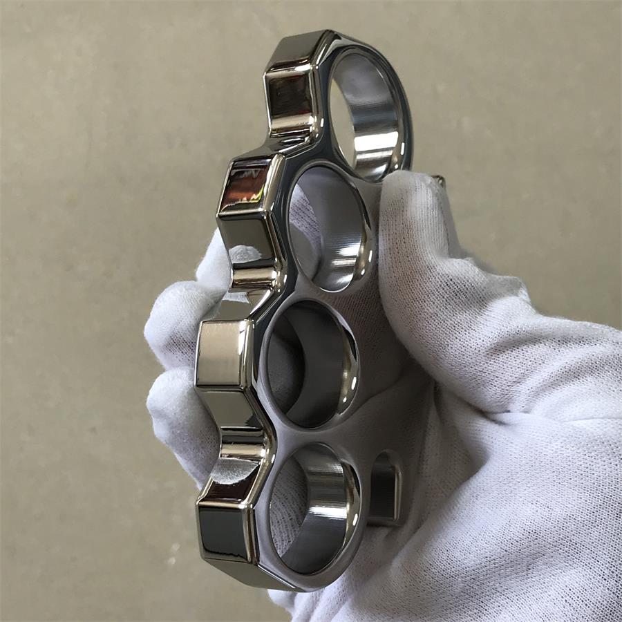 Vertical profile of the steel knuckle duster held in a gloved hand, showing the stepped knuckle edge and chamfered facets
