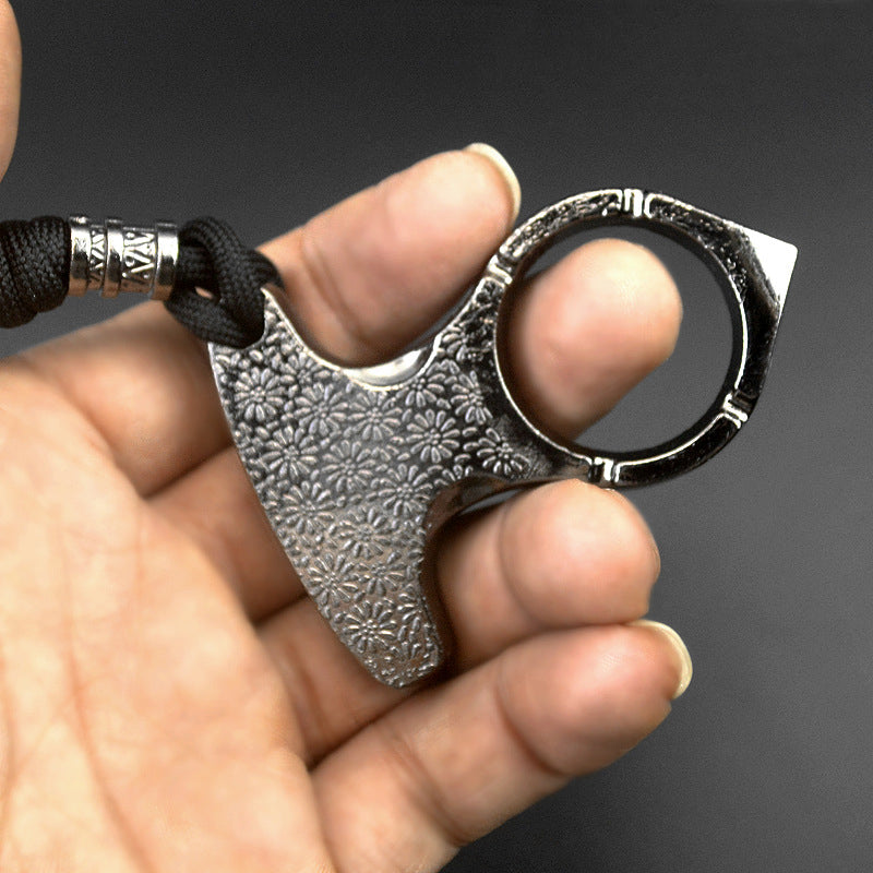 Angled view of the silver one finger knuckle outdoors showing the daisy embossing and polished notched finger ring with black paracord lanyard