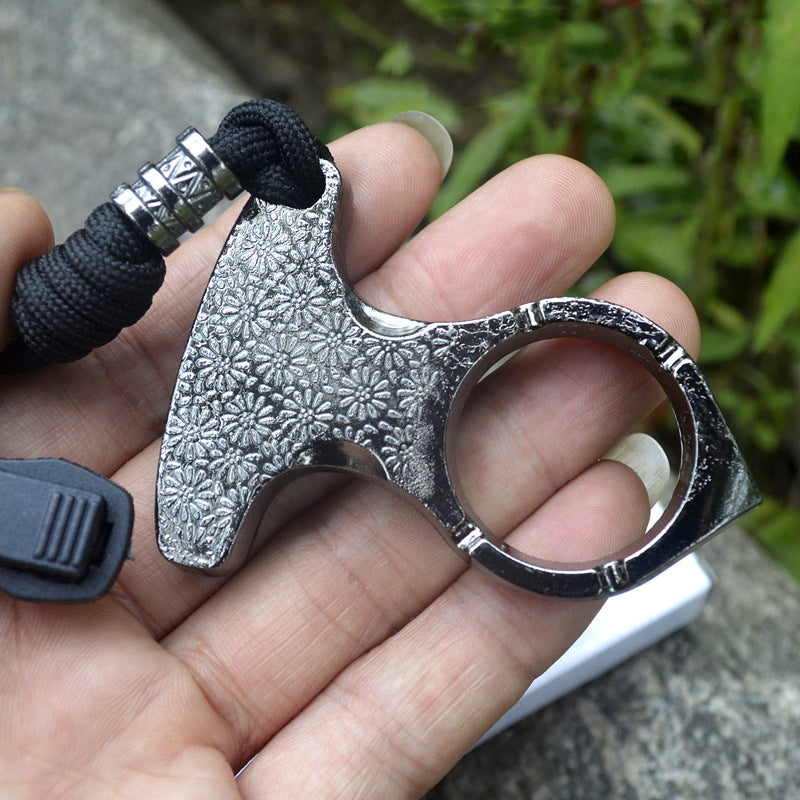 Close view of the one finger knuckle in hand showing the polished ring, embossed body and carved metal beads on the black paracord lanyard
