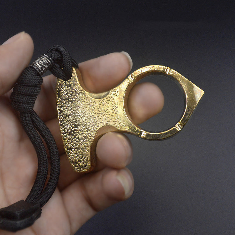 Gold colourway of the one finger knuckle duster held in a hand showing the embossed palm plate, round finger hole and black paracord lanyard