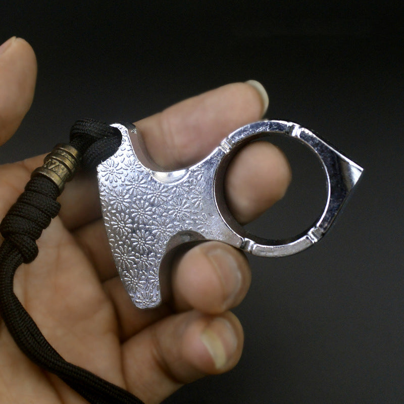 Hand holding the silver one finger knuckle duster with daisy-embossed palm plate, round finger hole and black paracord lanyard on a dark background