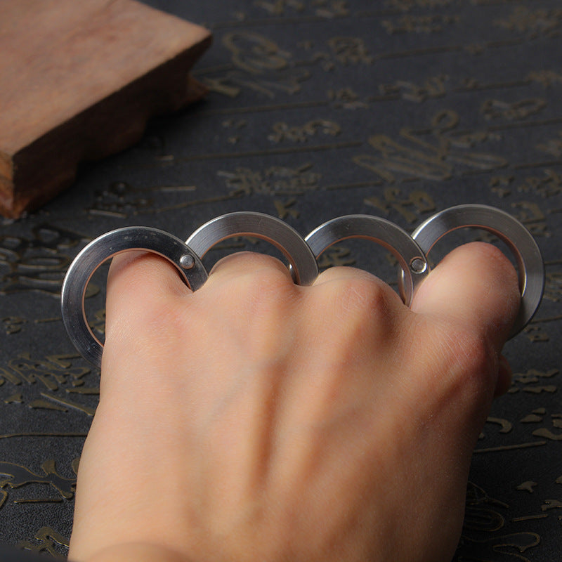 Open hand resting flat with the unfolded four-ring steel piece on the fingers over an engraved mat and wooden block