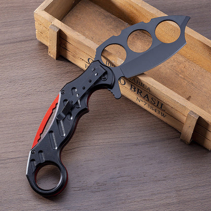 Open black folding knuckle knife resting on a wooden box