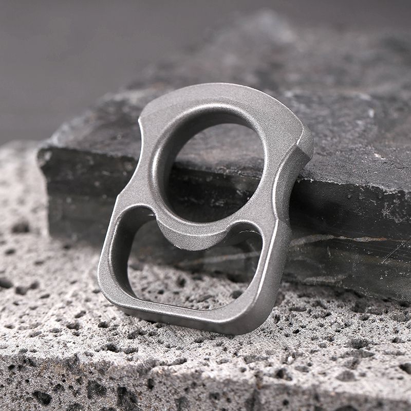Grey zinc alloy mini knuckle duster bottle opener standing upright on stone with its finger ring facing up