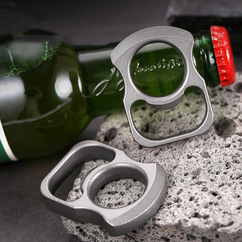 Two zinc alloy opener tools resting on porous stone beside a green bottle with a red crown cap