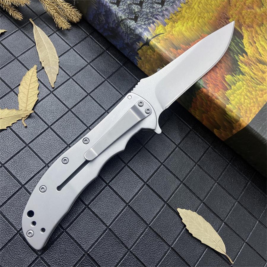 Open steel folding knife with pocket clip laid beside dried leaves and a printed gift box