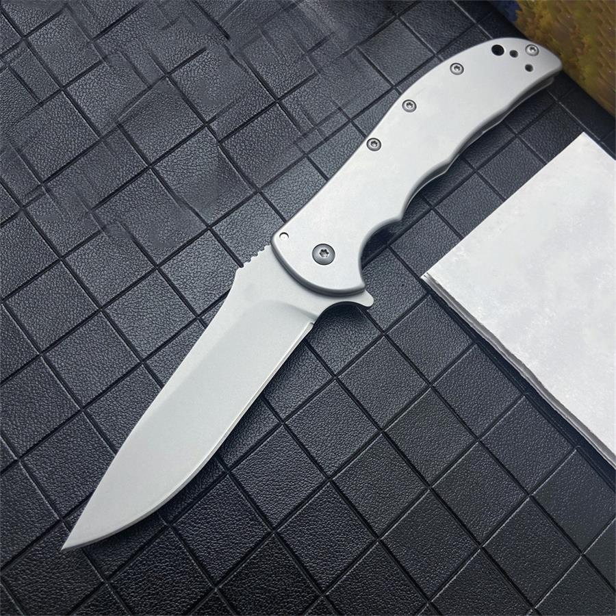 Open folding knife with silver steel handle and drop-point blade lying on a black grid-textured surface