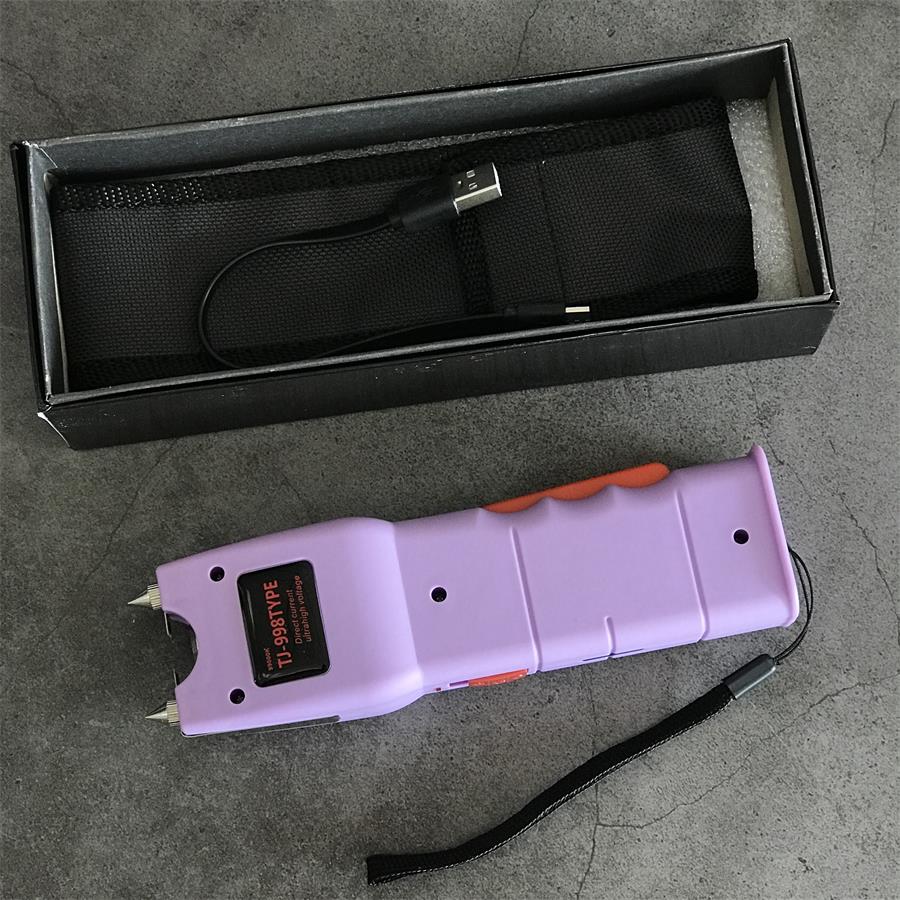 Open retail box with black holster and USB cable beside the light purple unit showing the tail charging port and wrist lanyard loop