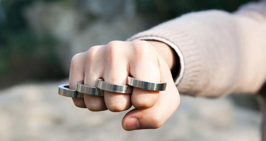 Outdoor shot of a fist wearing the stainless steel four-ring piece with blurred rocks and greenery in the background