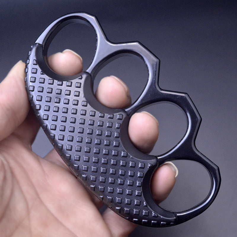 Open palm holding the all black knuckle duster with fingers threaded through the oval holes, dark background