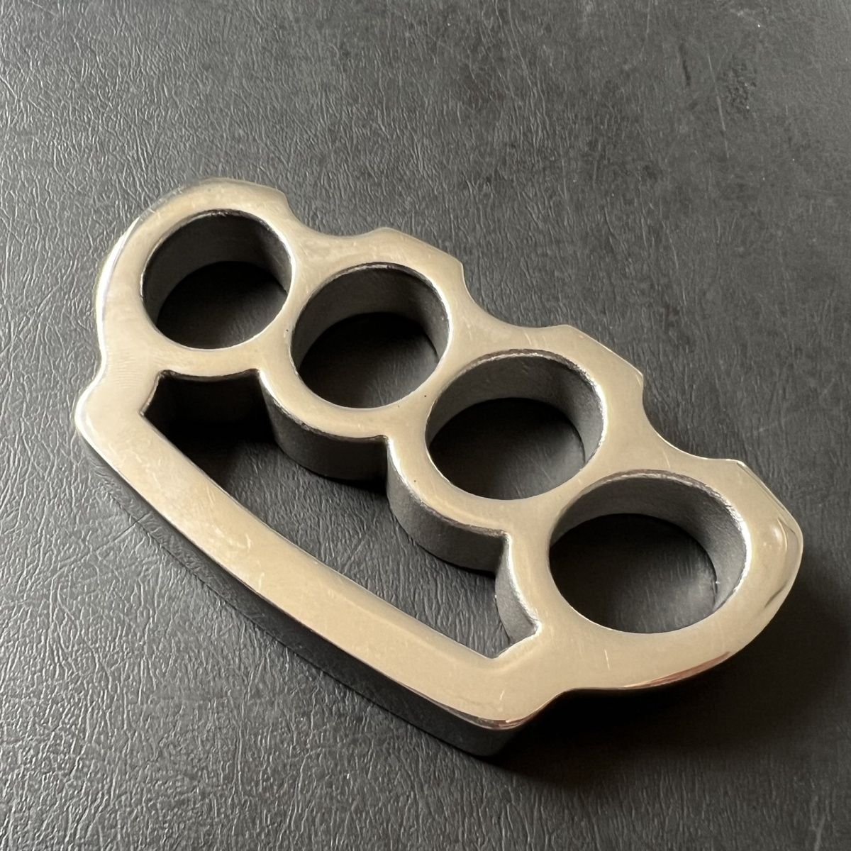 Angled view of the bare stainless steel parachute rope knuckle duster on black leather.