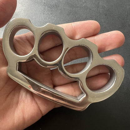 Bare stainless steel parachute rope knuckle duster held in a palm, showing the four-hole back side.