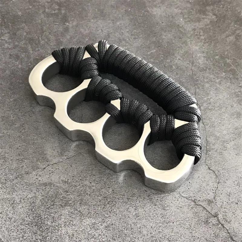 Stainless steel parachute rope knuckle duster with black cord wrap lying on gray concrete.