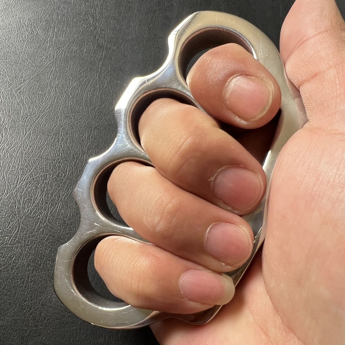 Hand gripping the stainless steel parachute rope knuckle duster with fingers through the holes.