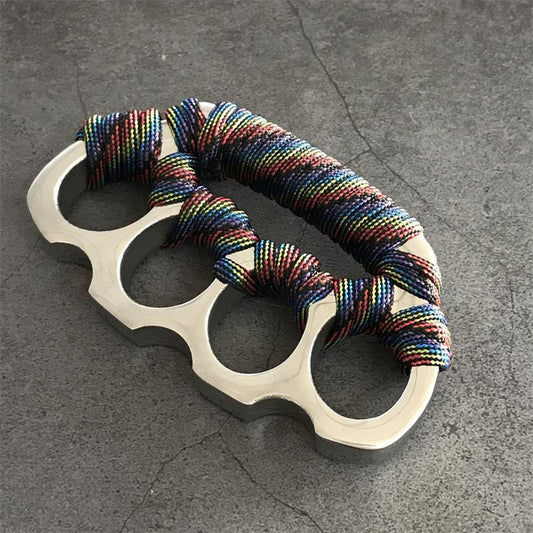 Stainless steel parachute rope knuckle duster with multicolor cord wrap lying on gray concrete.