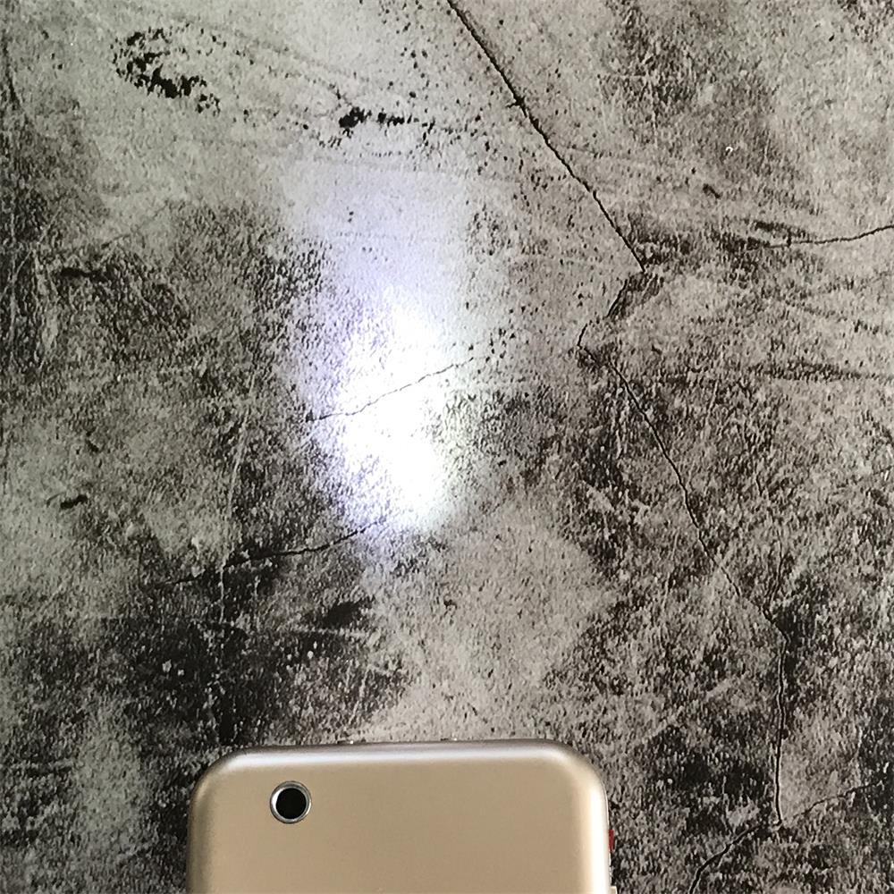 Bright LED beam shining from the gold phone-shaped device onto a mottled concrete wall with the top corner in frame