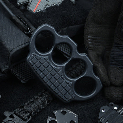 Black knuckle duster arranged in an EDC flat lay with a backpack, paracord and a multitool card