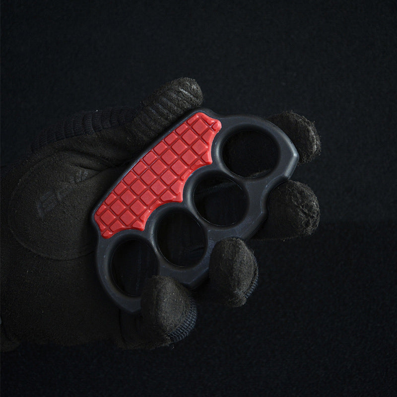 Black-gloved hand holding the red-black knuckle duster with its red grid panel facing up