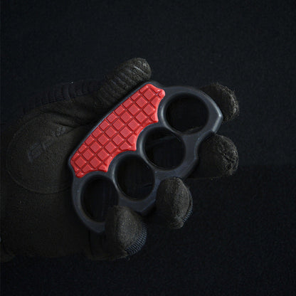 Black-gloved hand holding the red-black knuckle duster with its red grid panel facing up