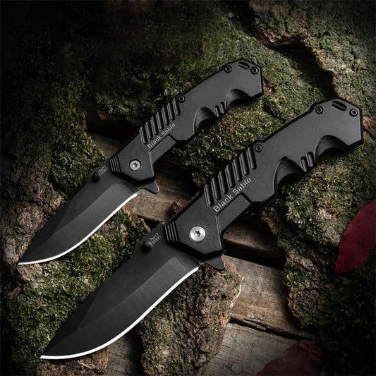 Two black folding outdoor knives on moss and wood background