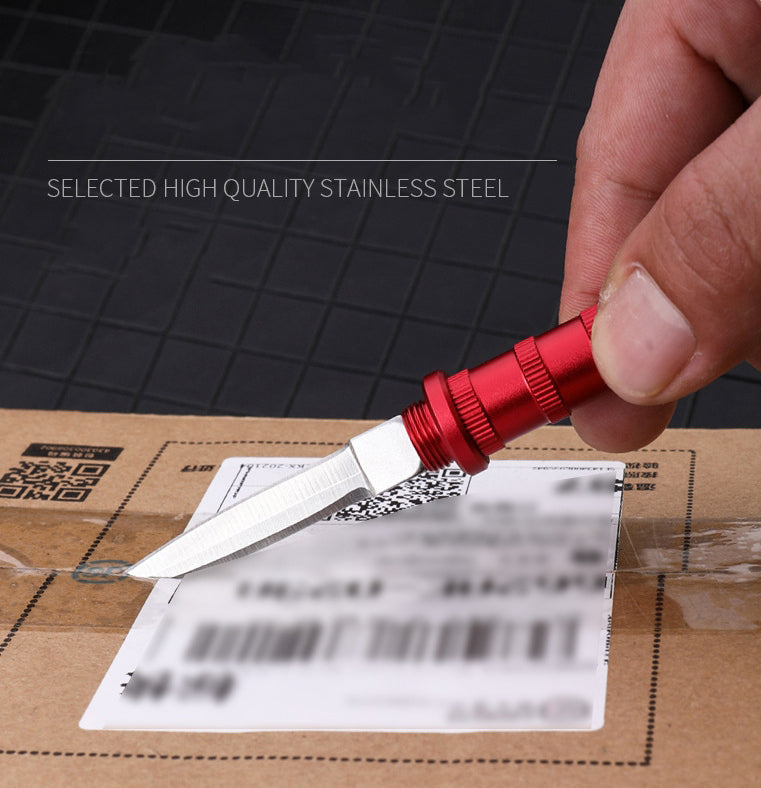 Red keychain dagger with the blade out, cutting tape on a cardboard box in a hand, reading 'Selected High Quality Stainless Steel'.