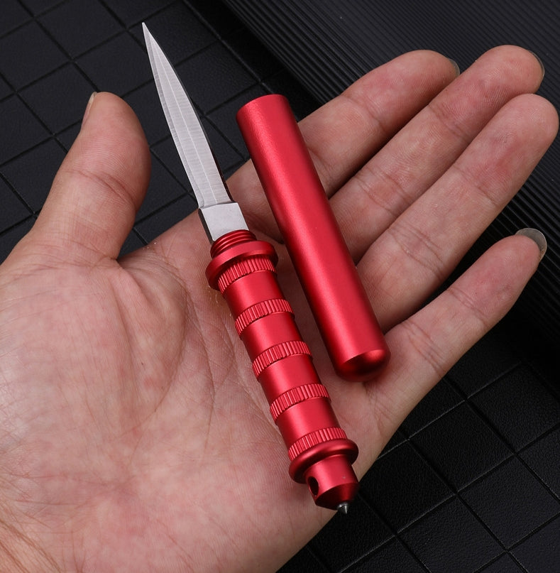 Red keychain dagger held in an open palm from above, blade exposed, ribbed handle with a tail window-break tip and a detached red scabbard beside it.
