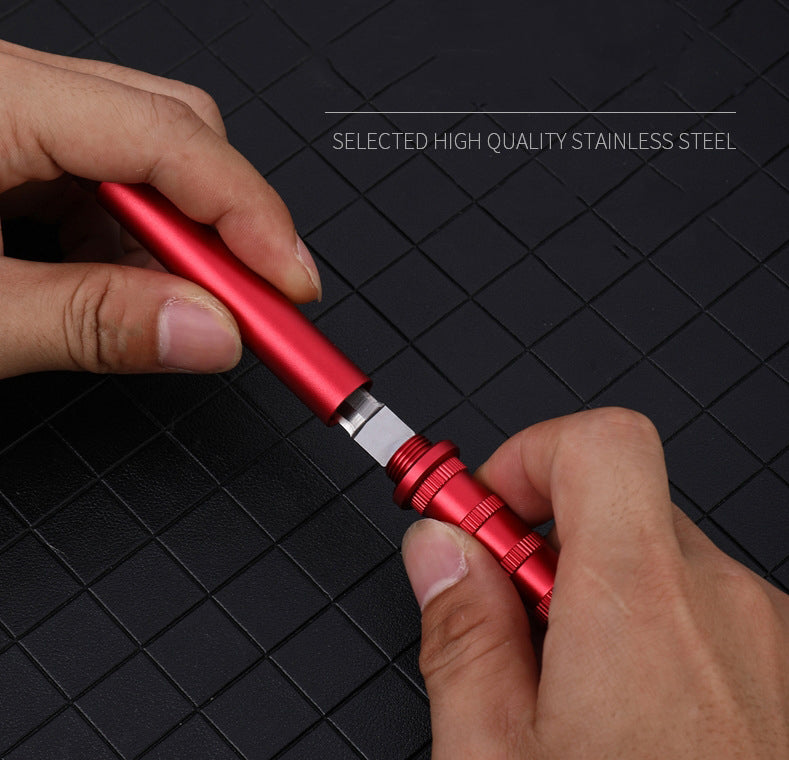 Red keychain dagger held by two hands, the blade partly out between the handle and the knurled cap, on a dark grid mat.