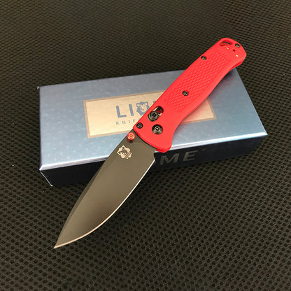 Red handled folding knife with black-coated drop-point blade open across a Liome branded box
